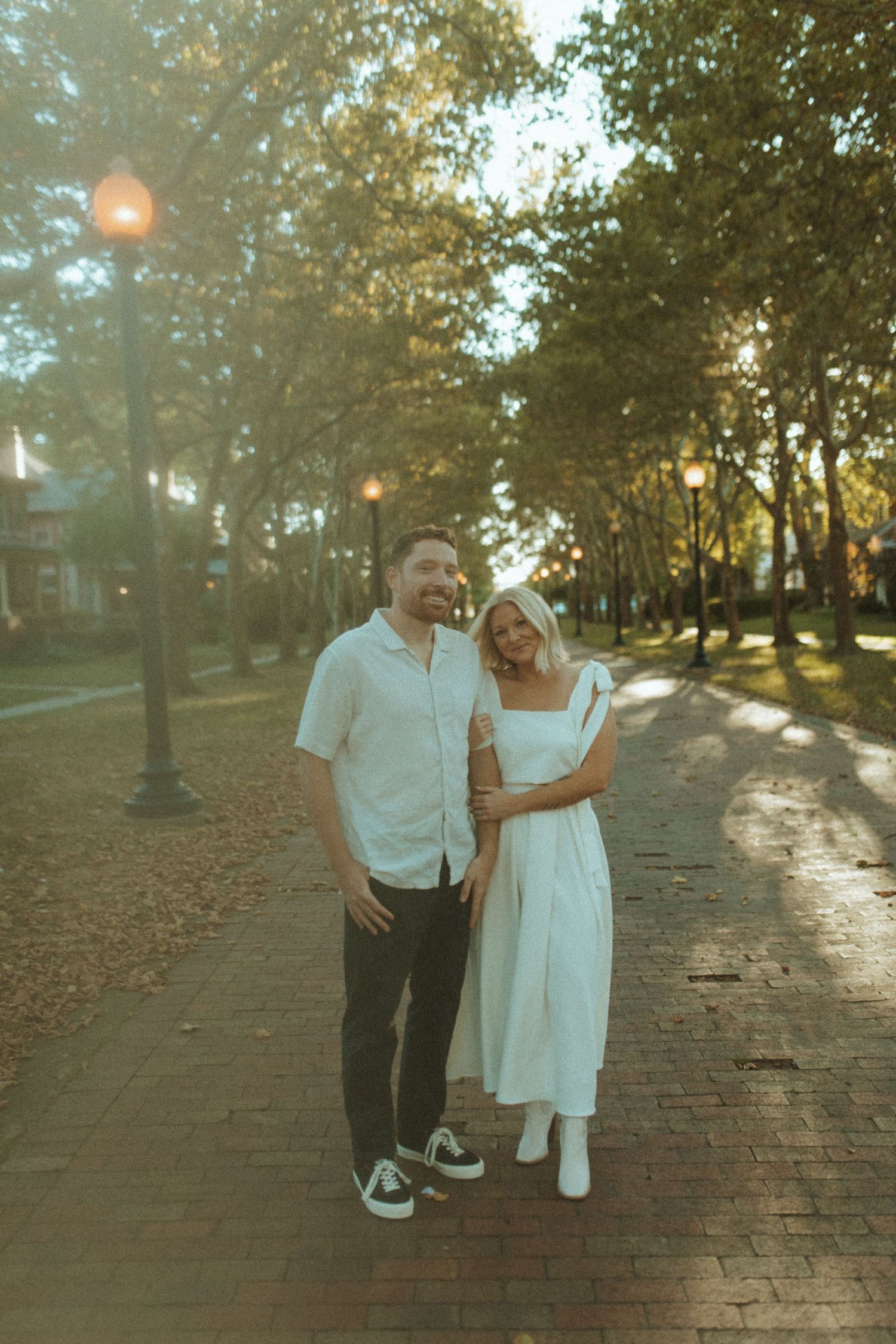 Couple shares joyful moment together on brick pathway with autumn trees and streetlamps.