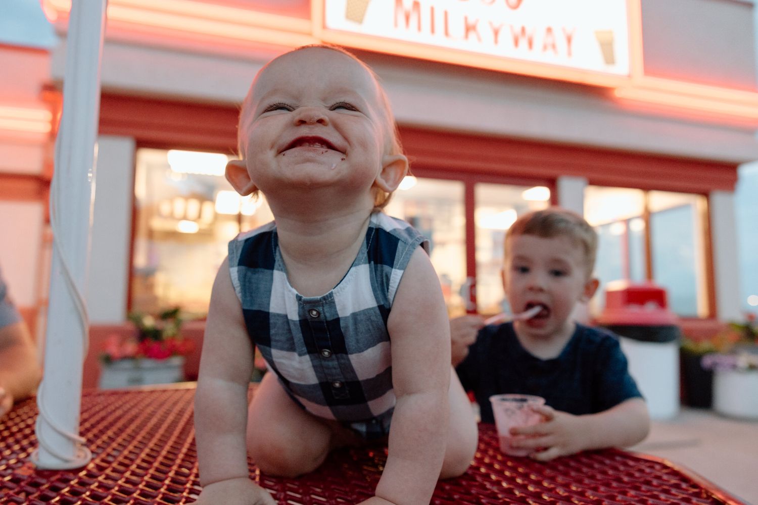 Children smiling at outdoor restaurant table with Milkyway sign glowing in background.