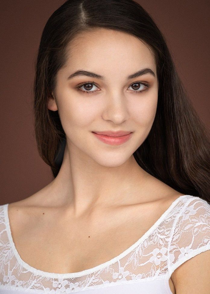 Portrait of a young woman wearing white lace top against brown background.