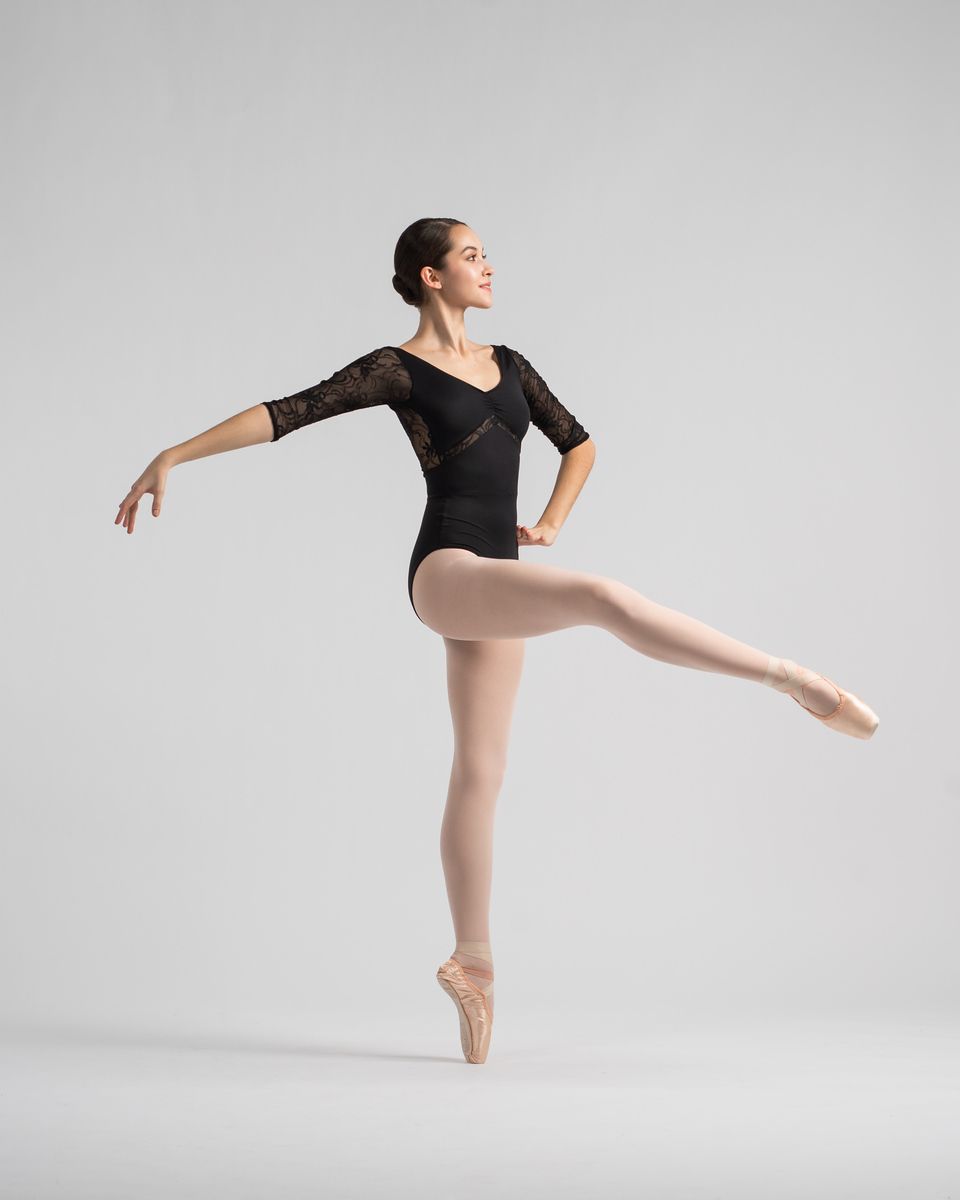 Dancer in black lace leotard performs elegant ballet pose on pointe in studio setting.