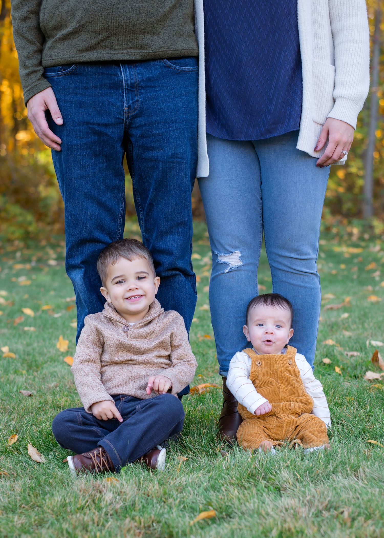 Two young children sit at their parents' feet during an outdoor autumn photo session.