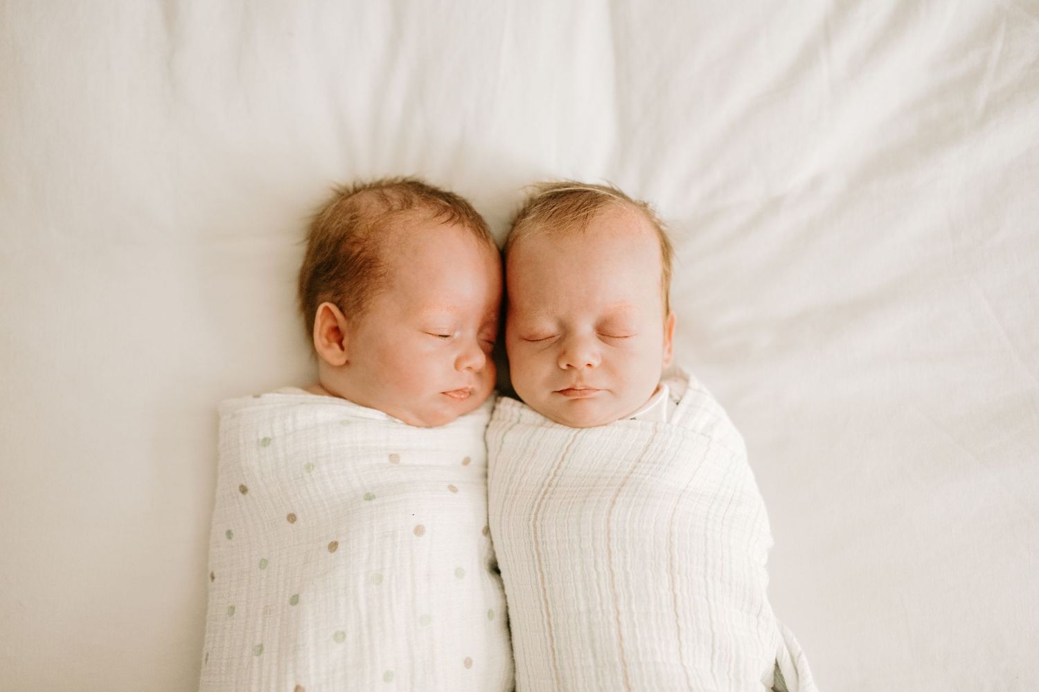 Twin babies photographed at their in-home newborn session. They are swaddled and snuggled right next to each other.
