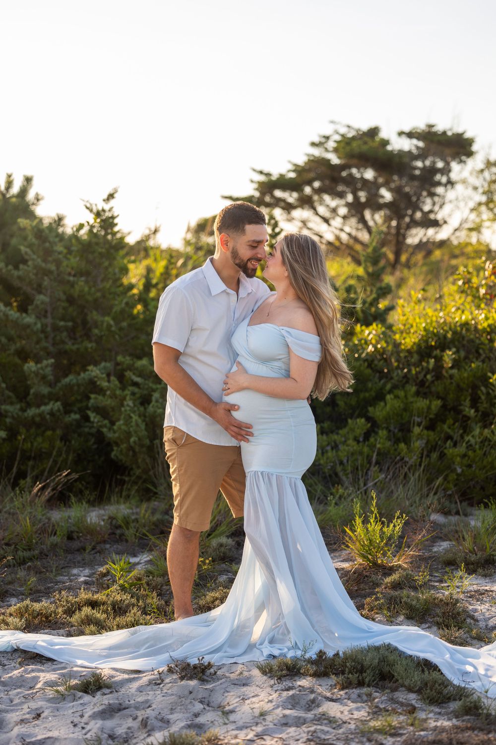 A couple shares a tender moment on the beach during a maternity photoshoot at golden hour.