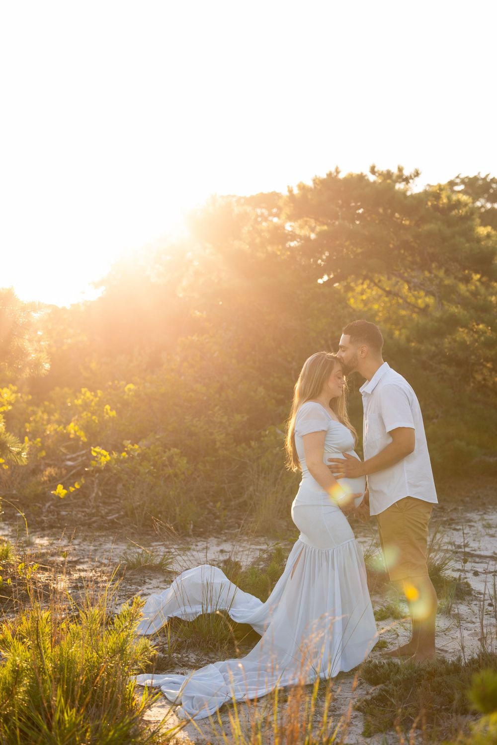 Sunset maternity photoshoot featuring a couple in white and khaki amid coastal scenery.