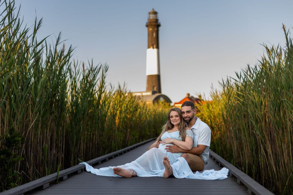 Maternity photo of couple sitting in boat with Fire Island Lighthouse in background.
