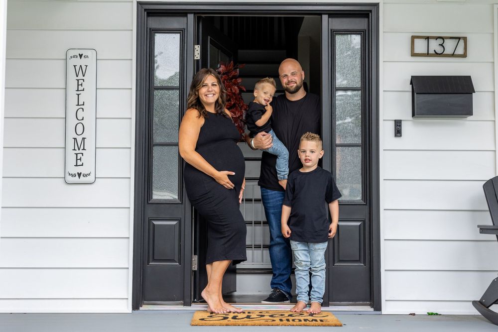 A family poses together in the doorway of their modern white house with black trim.