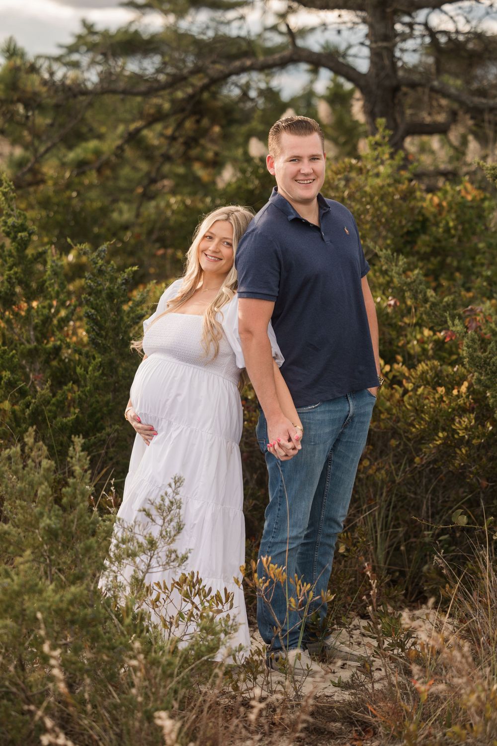 Outdoor maternity portrait of a couple standing among natural foliage.