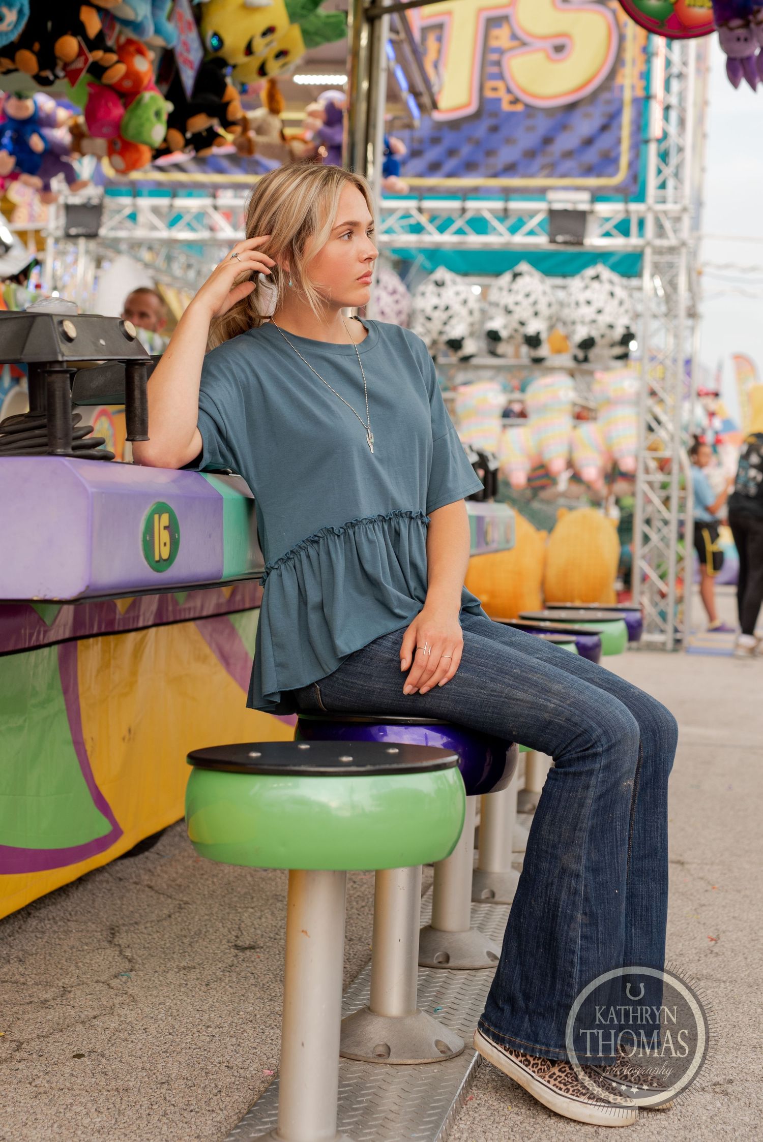 Person sitting on carnival game stool wearing blue peplum top and flared jeans.