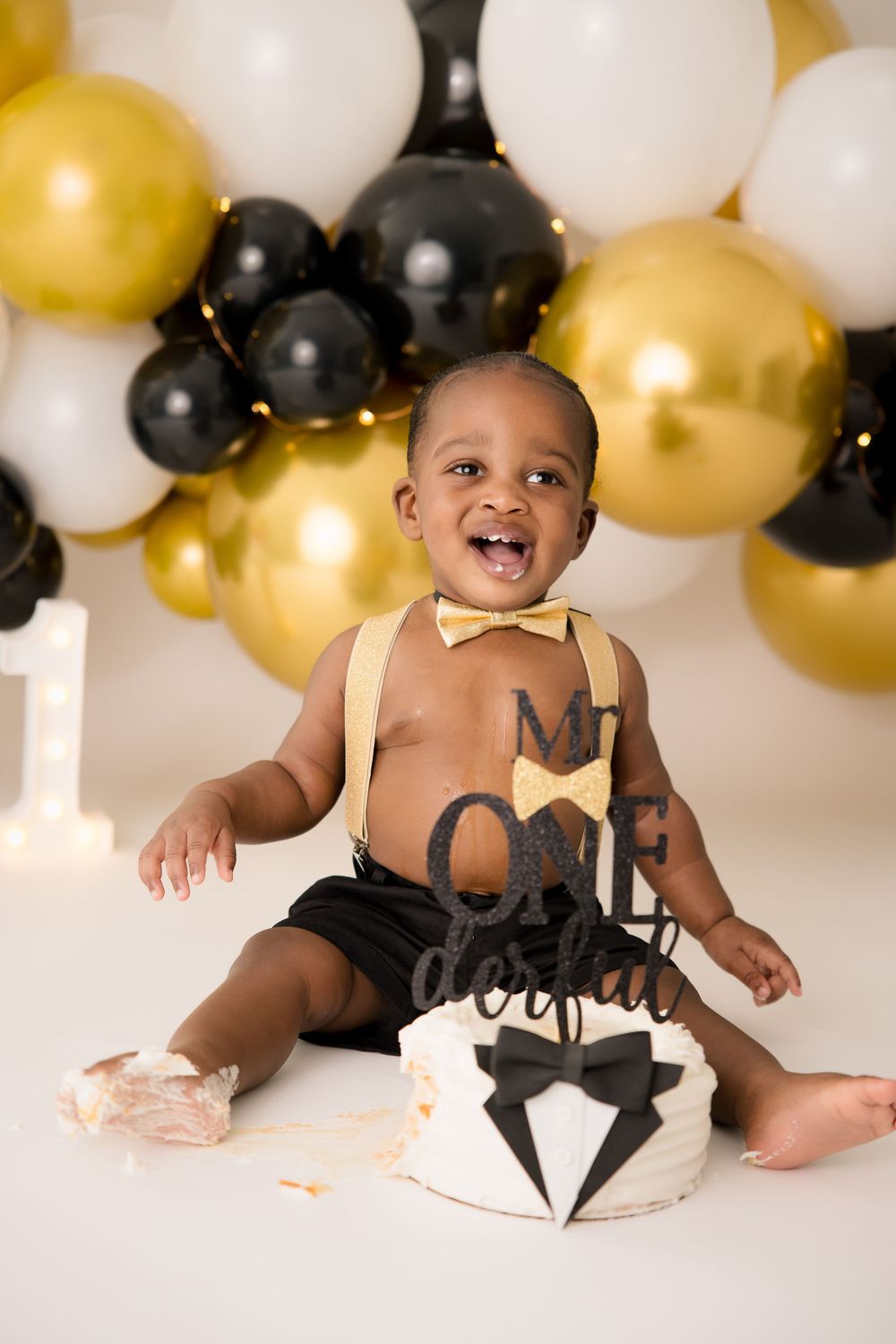 Baby enjoying cake smash session with gold and black balloon decorations.