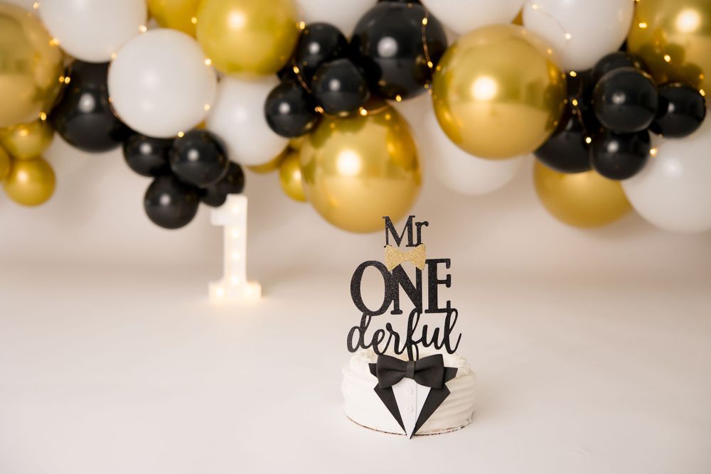Elegant cake topper reading Mr One-derful with black and gold balloon arch.