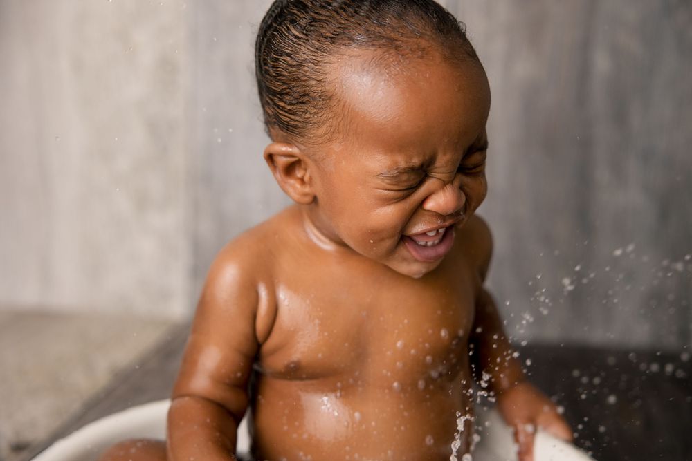 Baby splashing and laughing joyfully during bath time with water droplets in the air.
