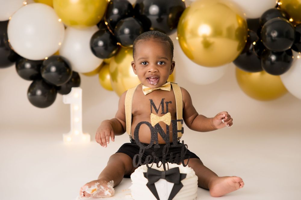 Baby sitting with smash cake during first birthday photoshoot with balloon backdrop.