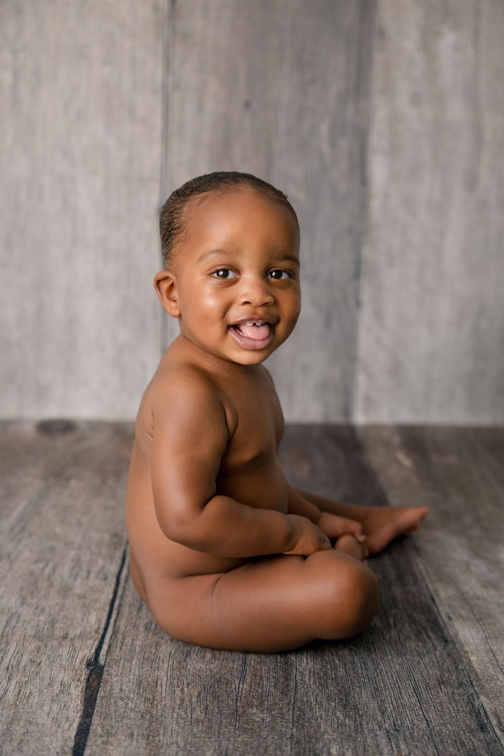 Baby with joyful expression sitting on rustic wooden floor.