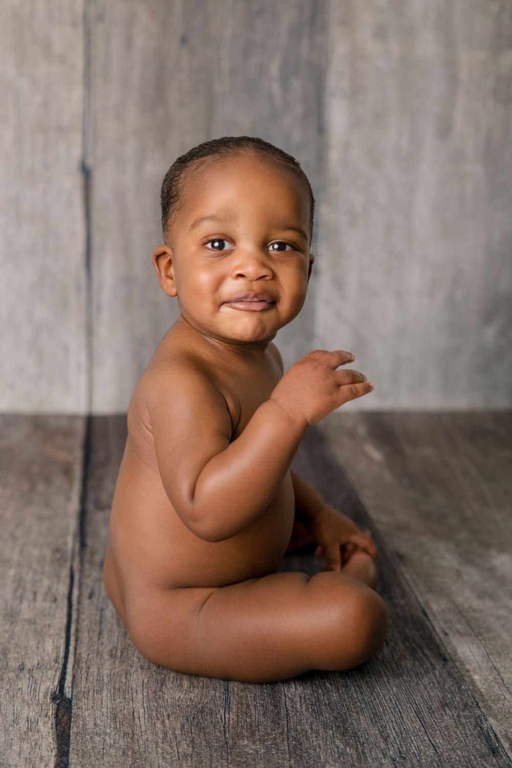 Portrait of smiling baby sitting on wooden floor during minimalist photo session.