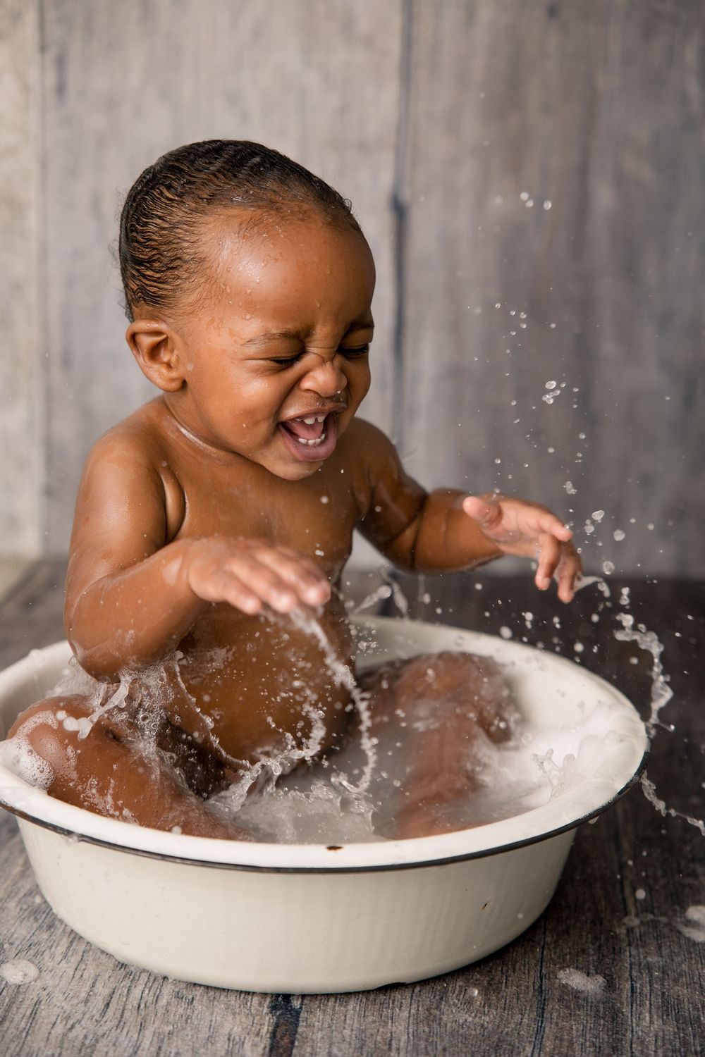 Baby creates water splashes while playing in a white basin during a photo session.
