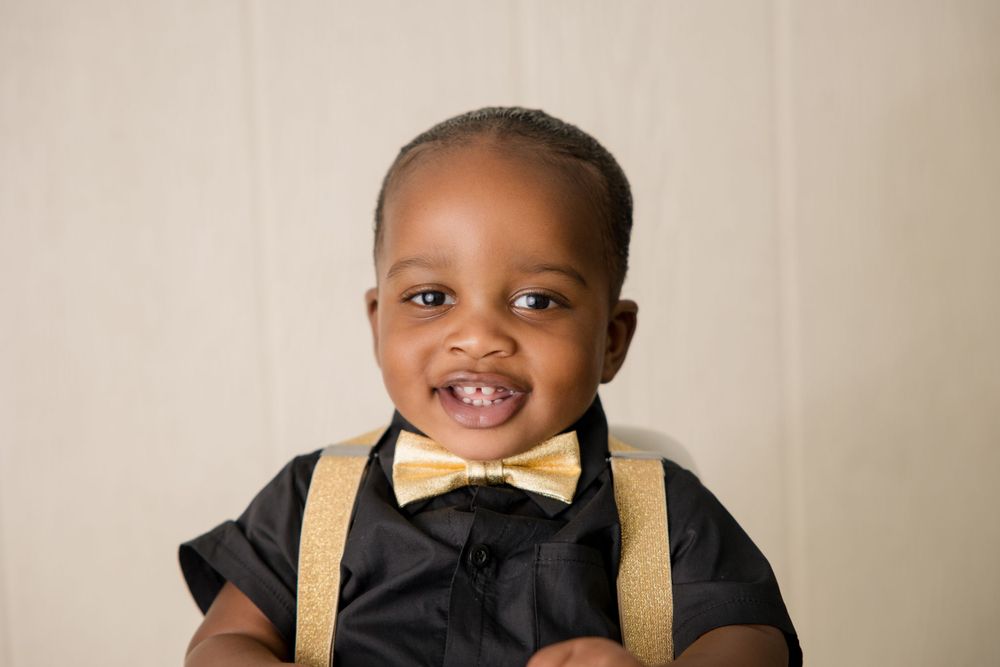 Baby wearing black dress shirt with yellow bow tie and suspenders for formal portrait.