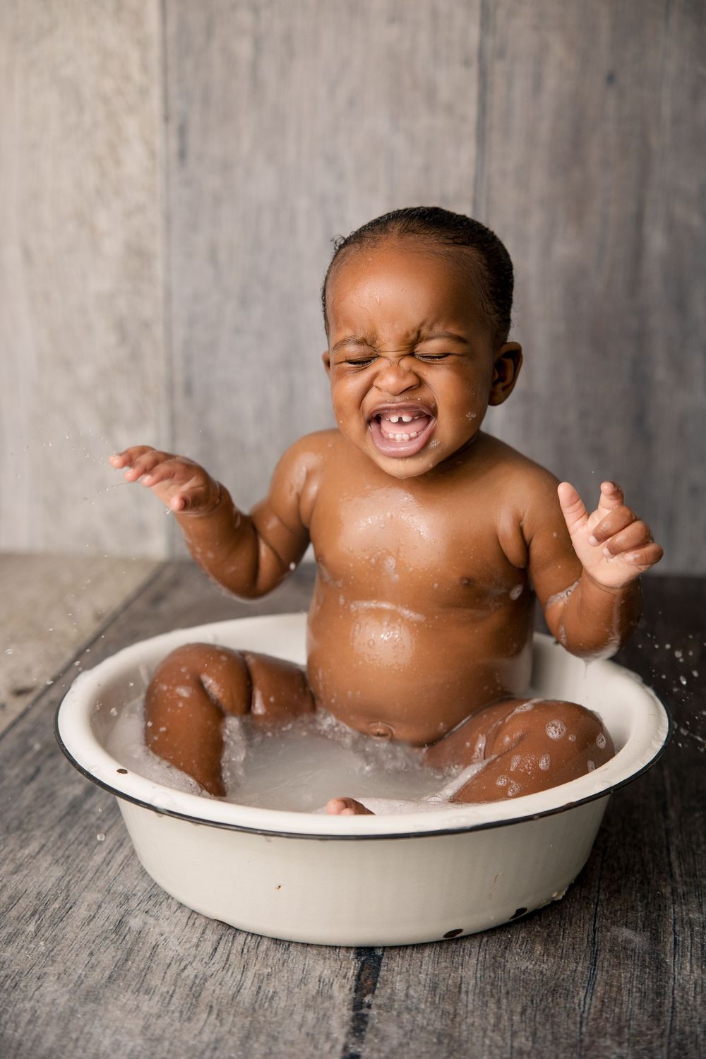 Laughing baby sits in soapy water during a playful bath photoshoot.