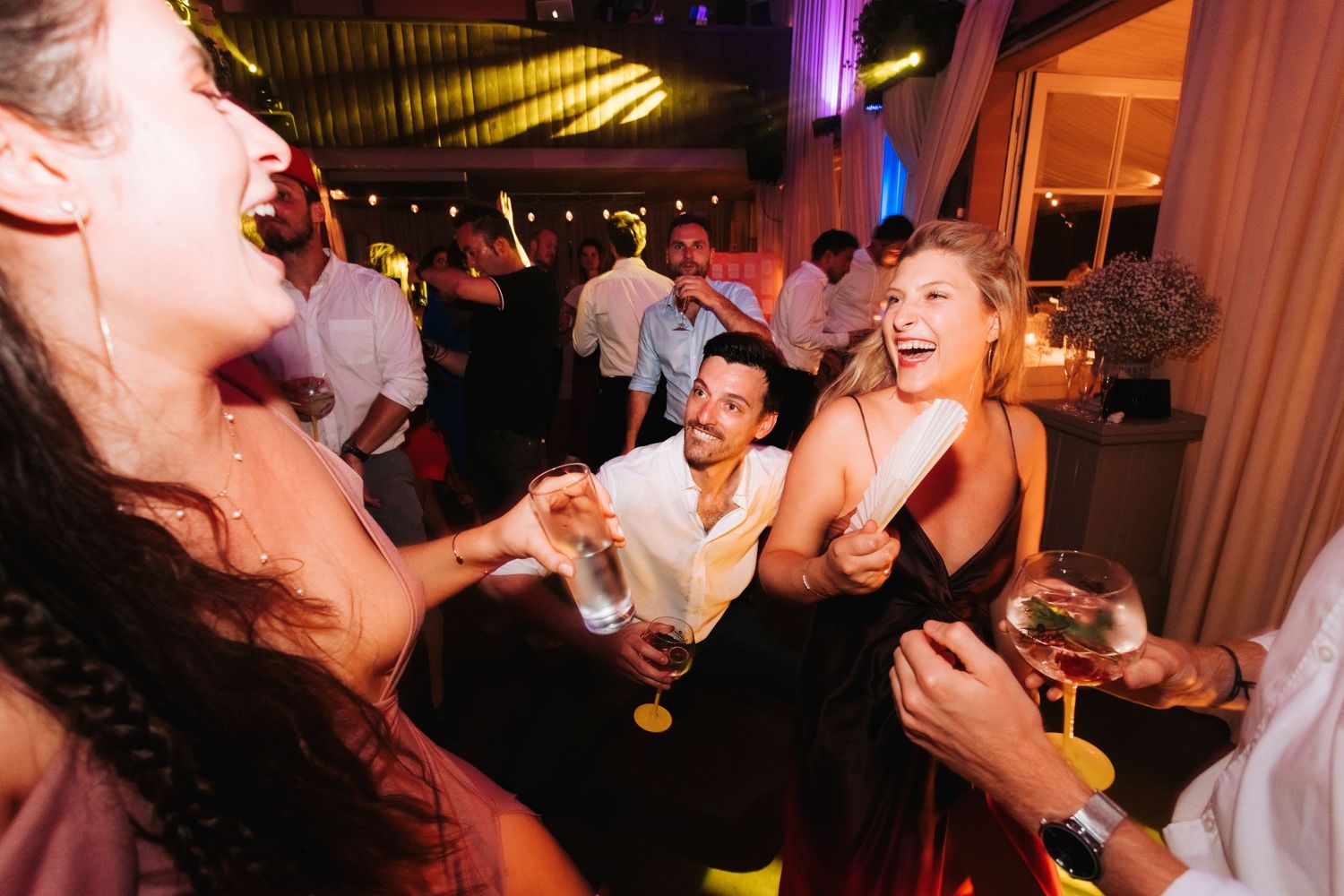 Lively party scene with people dancing and laughing under warm lighting at a nighttime celebration.