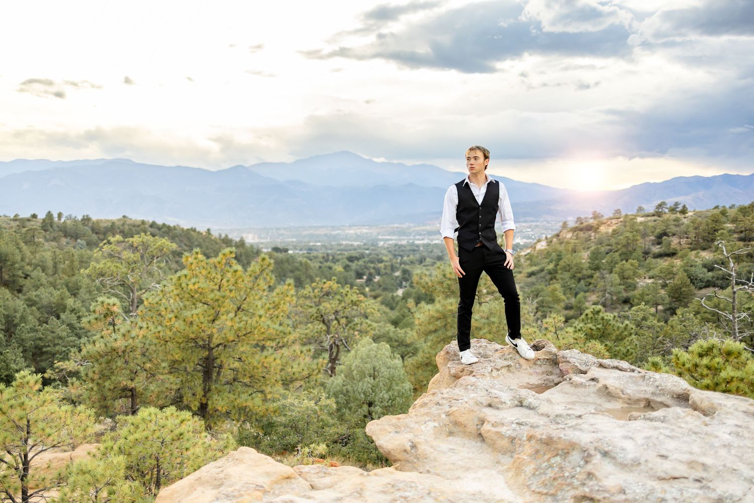 Senior guy stands on the rocks at sunset with hands in pockets at his senior session at Palmer Park in Colorado Springs.