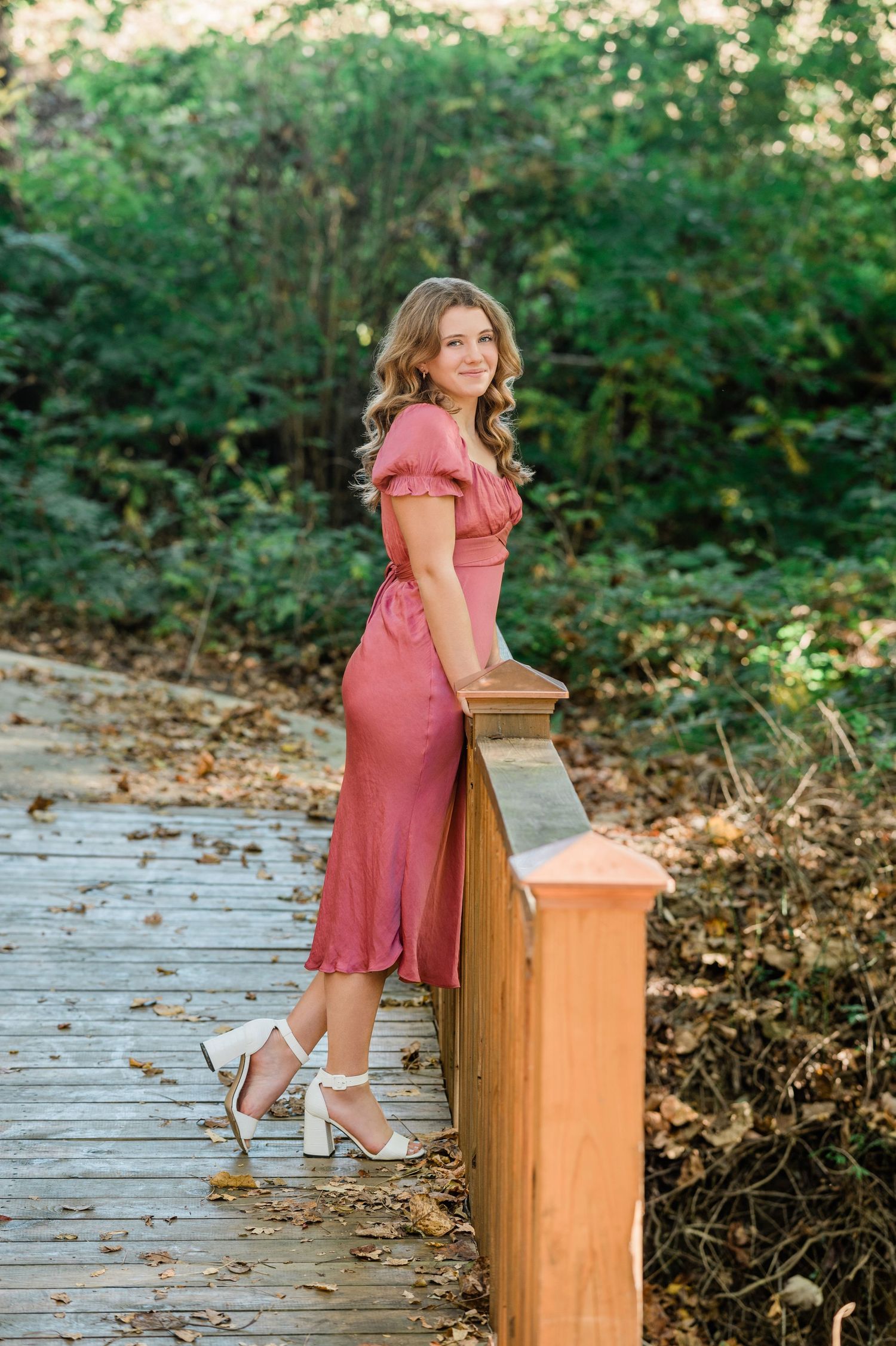 Elegant coral dress photoshoot on wooden deck surrounded by lush forest scenery.