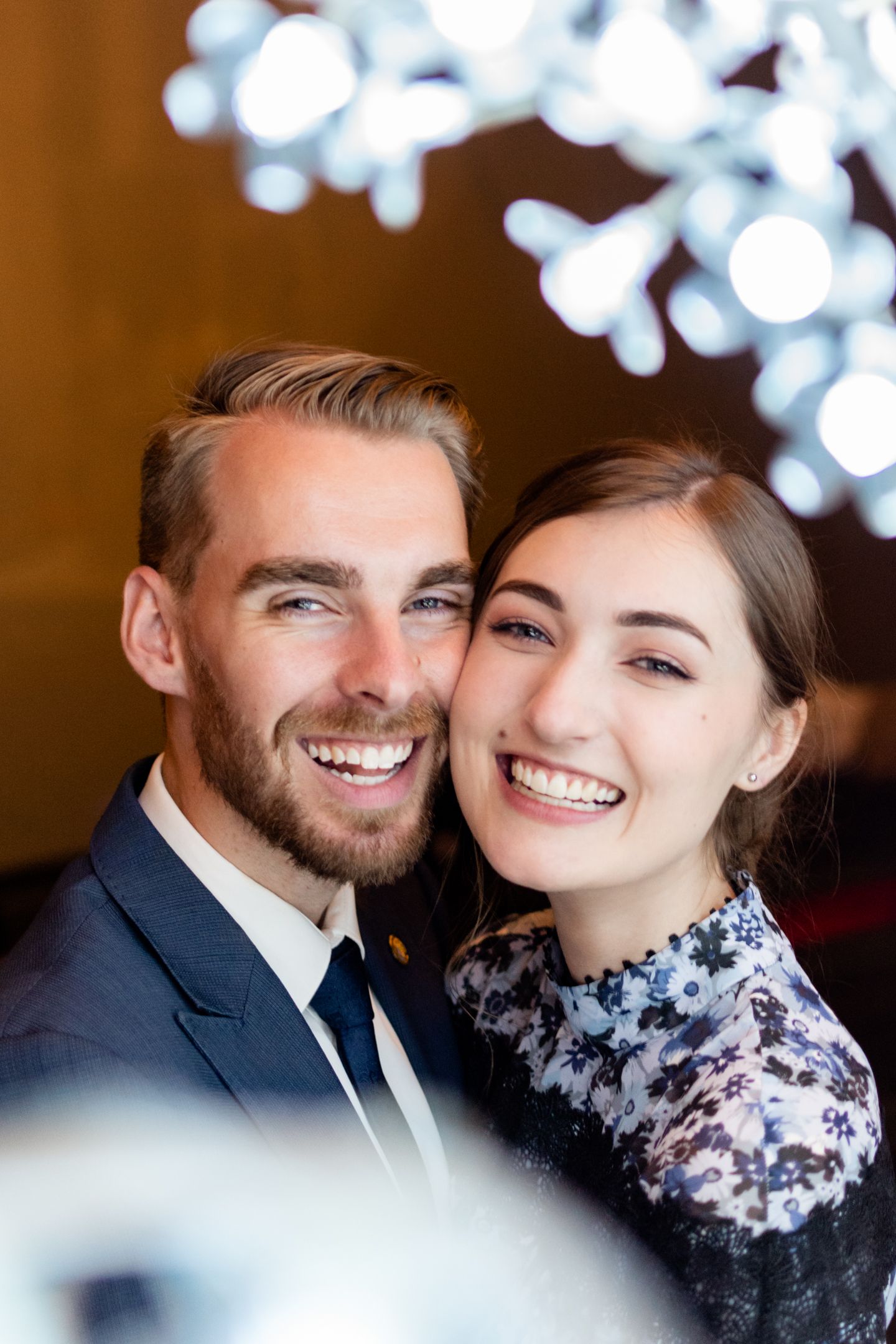 A romantic portrait of a couple in formal attire with bokeh lights in the background.