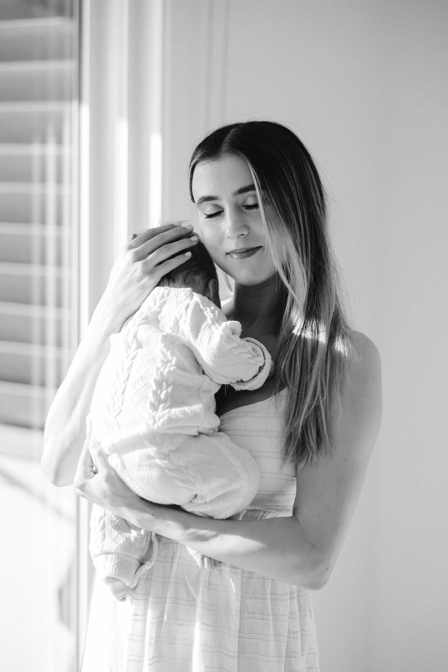 Black and white portrait of tender moment between parent and infant in white clothing.