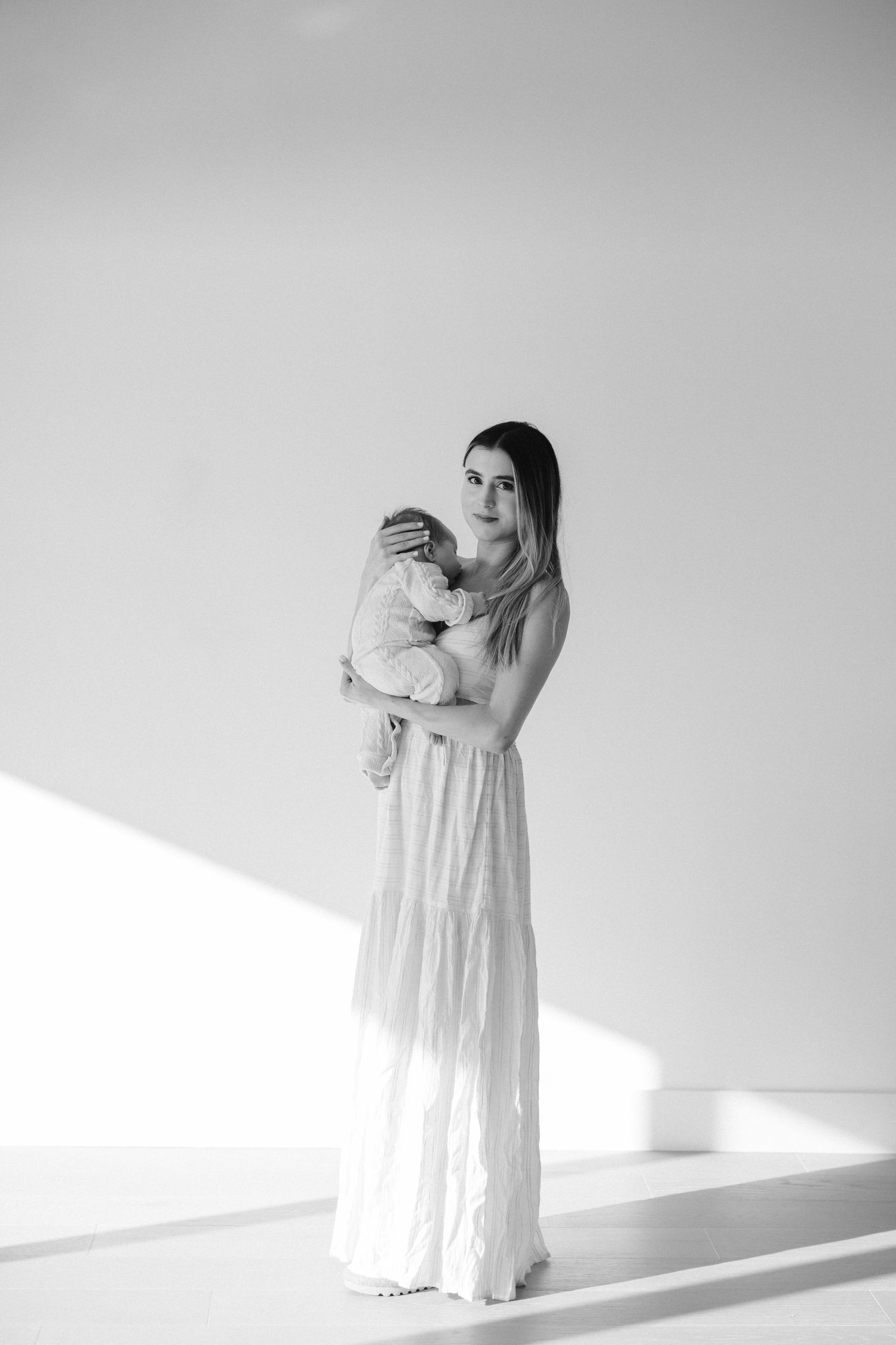 A tender moment captured in black and white as a figure in a flowing white dress cradles an infant.