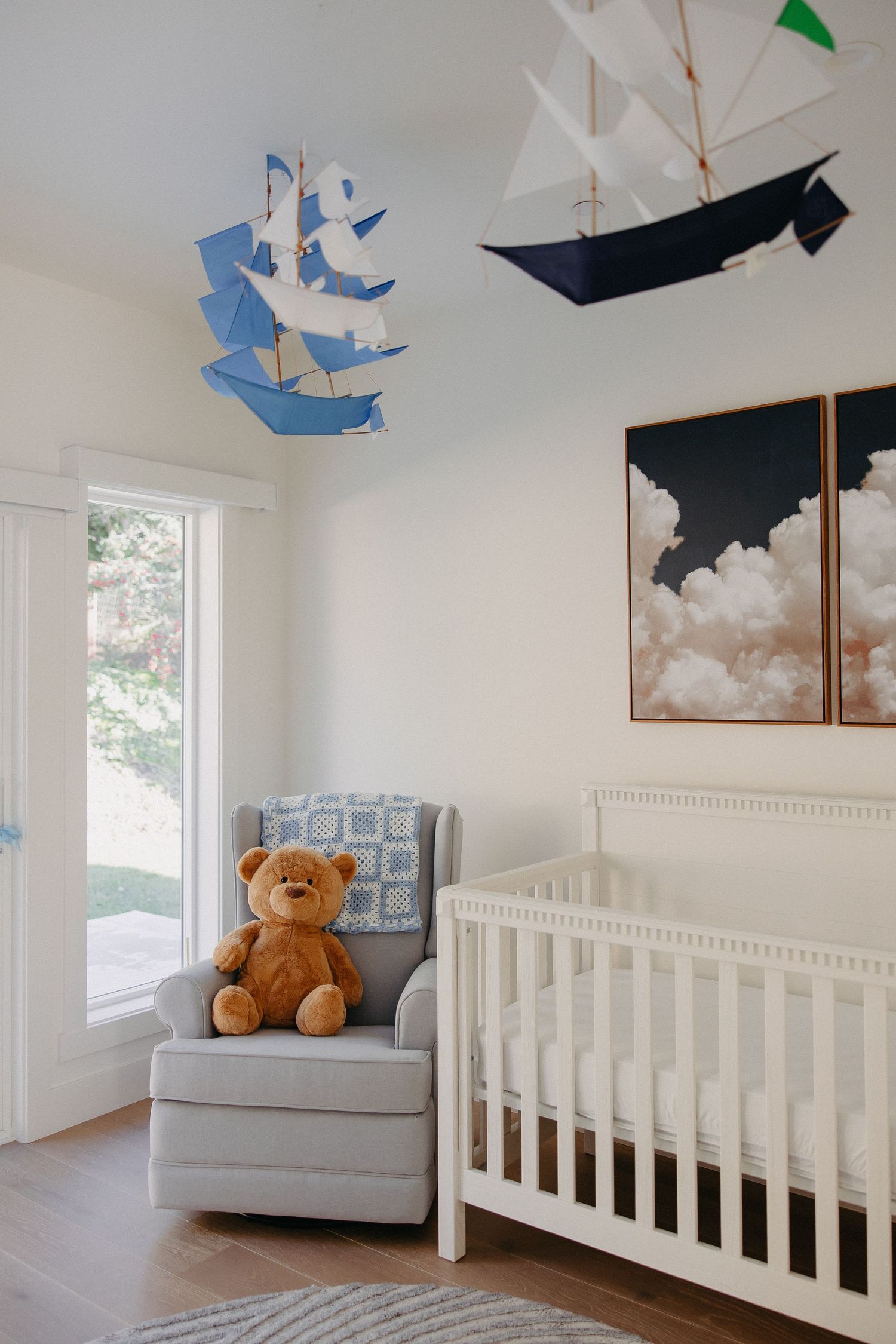 Nursery room with white crib, teddy bear on chair, and hanging nautical-themed mobile decorations.