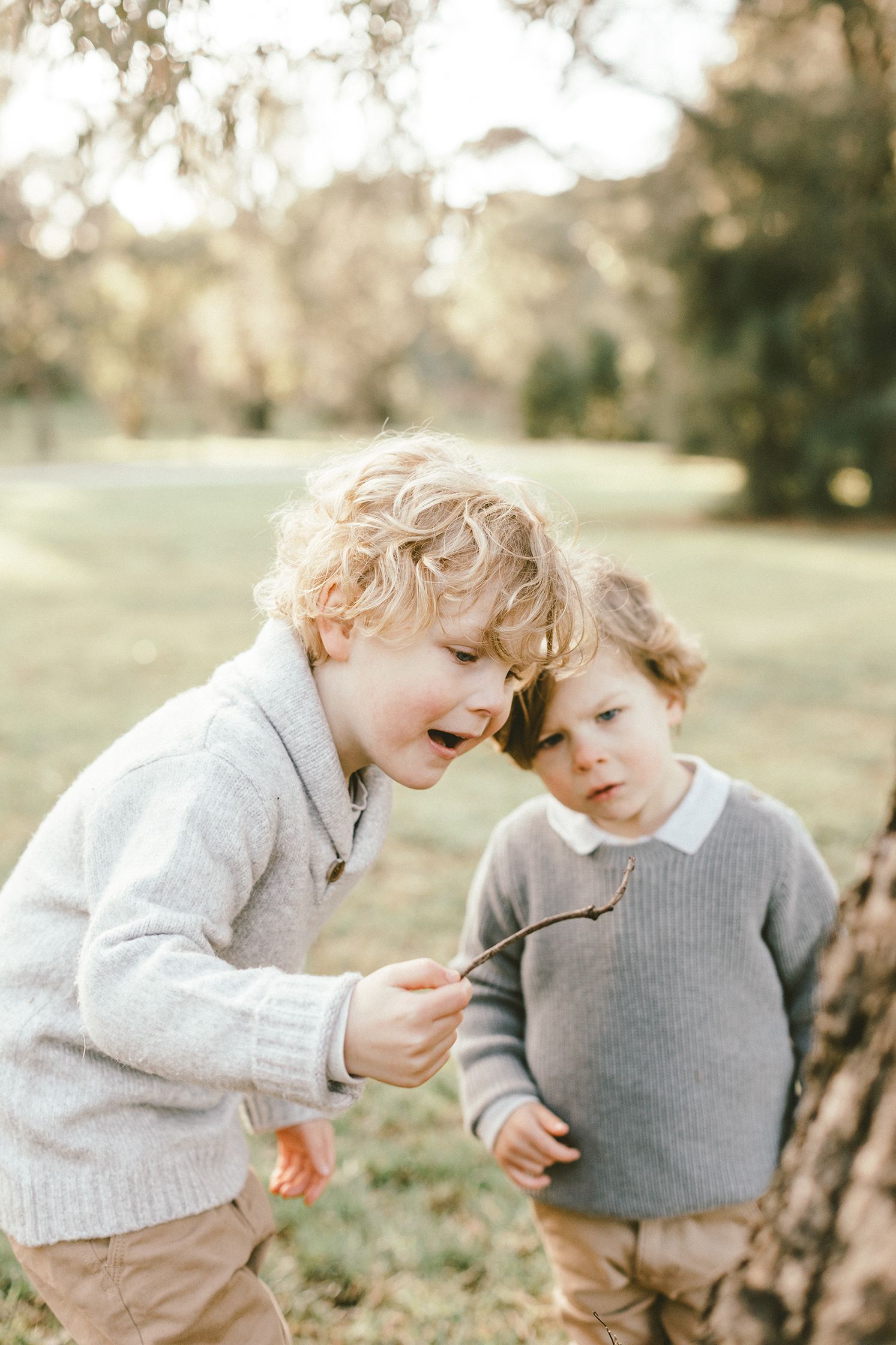 Two young children in grey sweaters share a tender moment while examining something together.