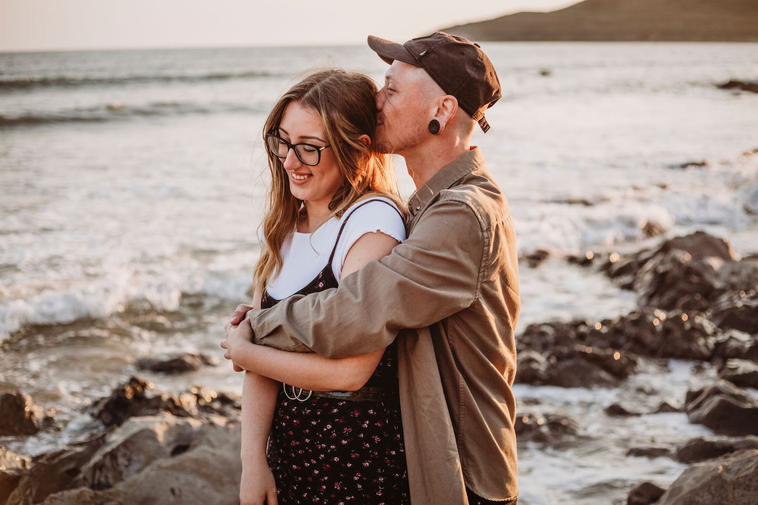 Romantic couple embracing on rocky beach at sunset.