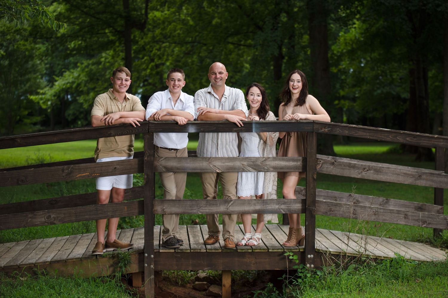 Family group photo session on a rustic wooden fence in a peaceful park setting.