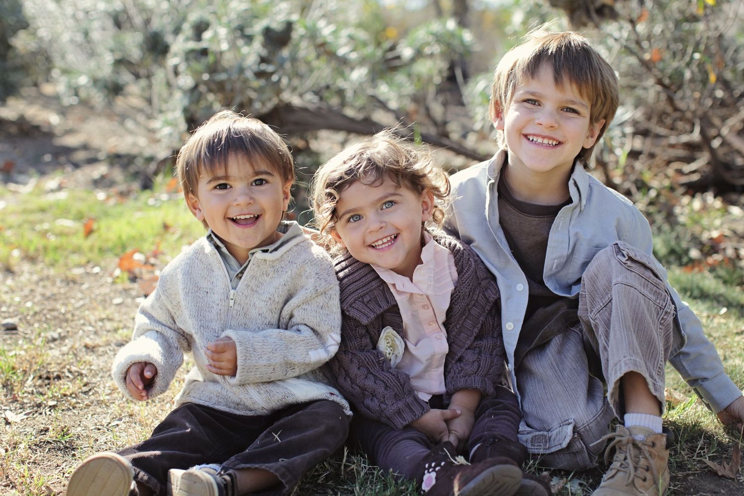 Three siblings sitting together outdoors sharing happy laughter.
