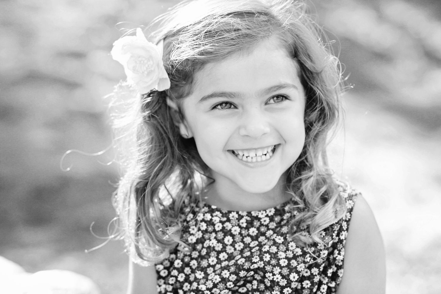 Black and white portrait of a child with flowing hair in floral dress.