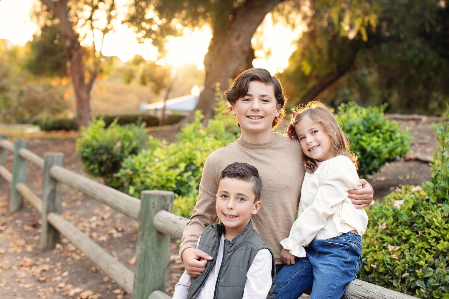Three children smiling together outdoors against natural background.