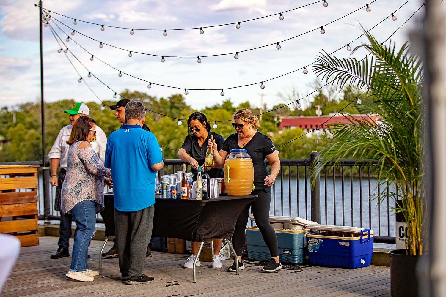 Outdoor party setup with string lights and bar service near waterfront.