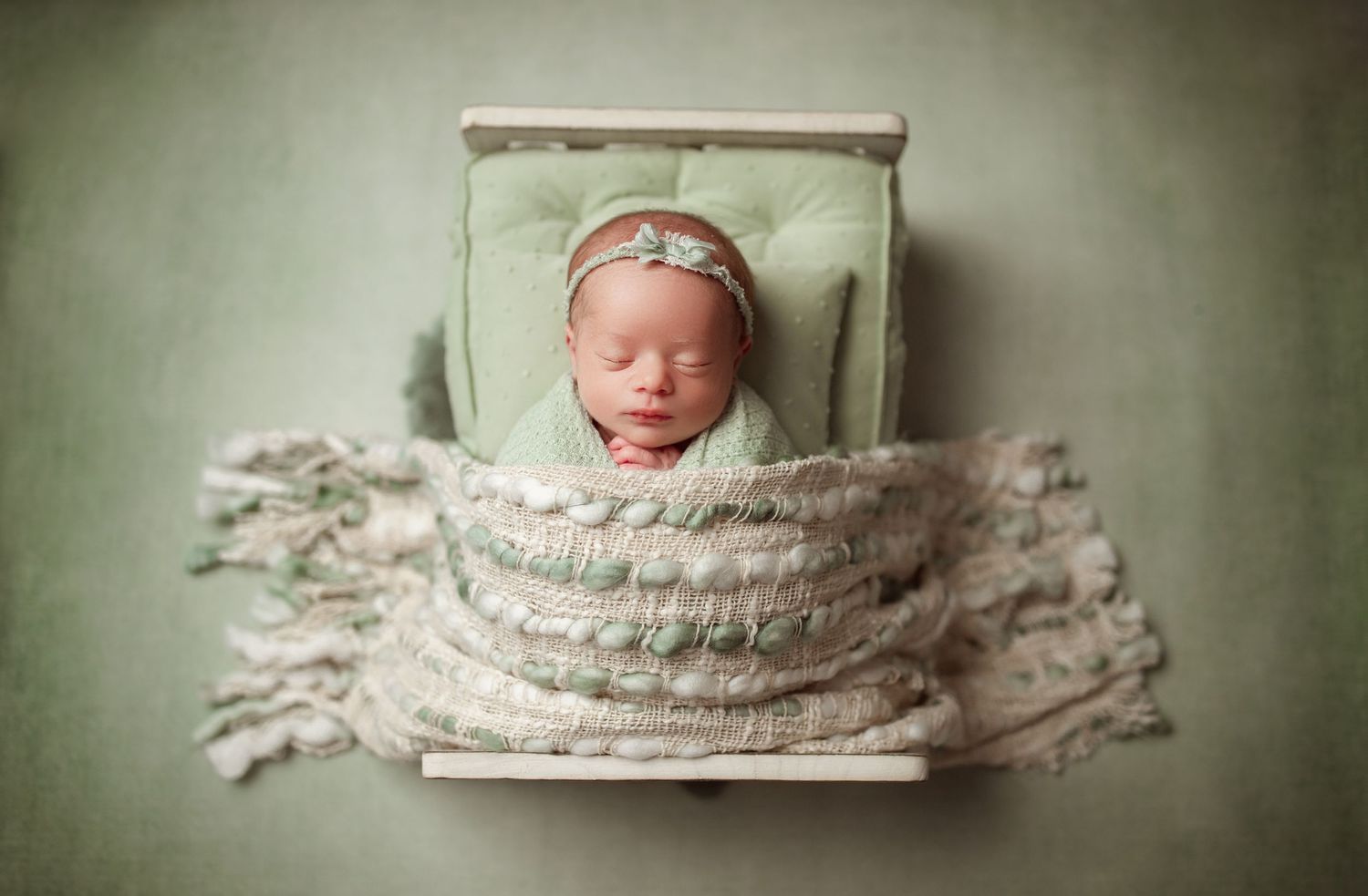 Sleeping newborn wrapped in textured blanket on mint green backdrop.