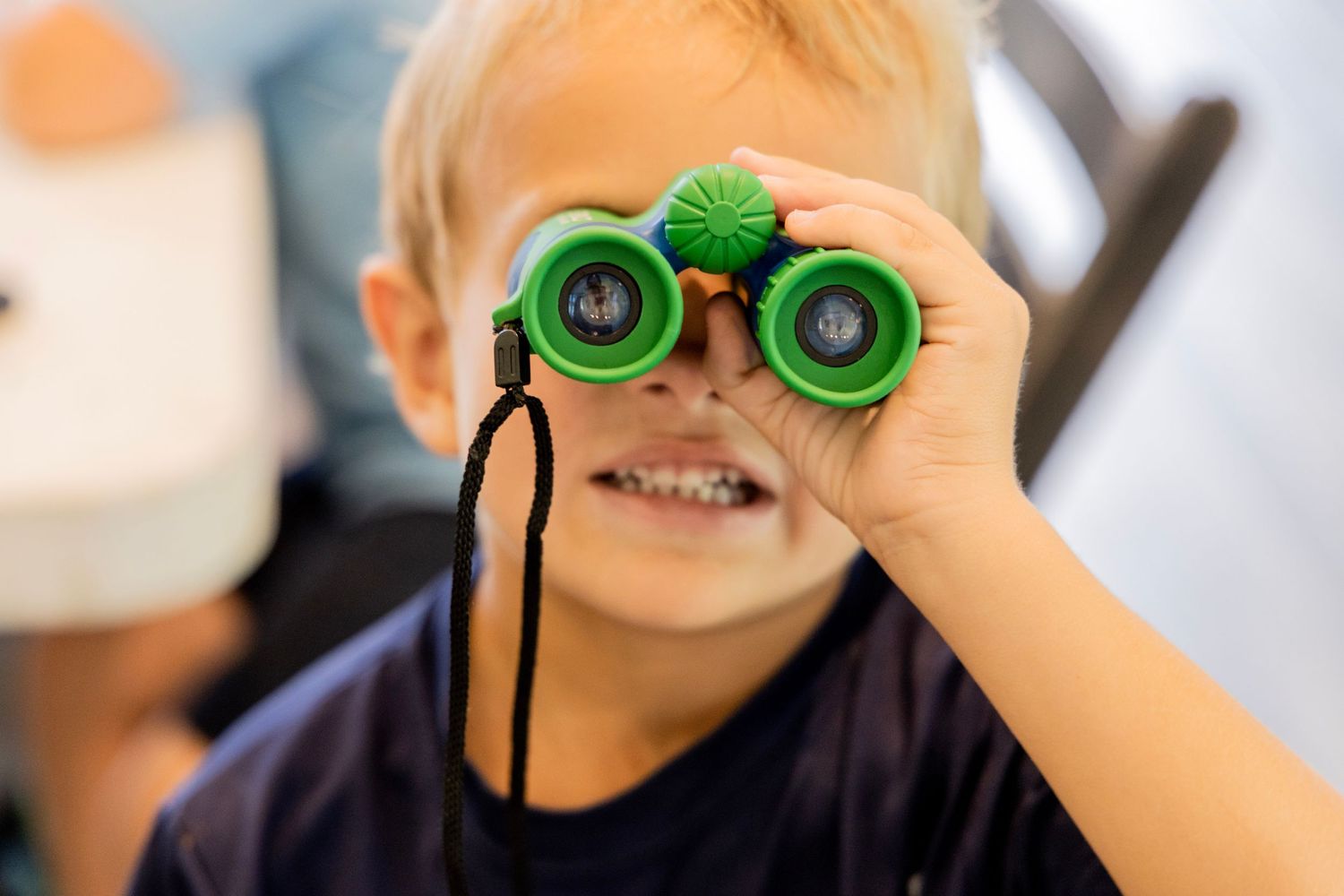 Young child smiling while looking through bright green toy binoculars.