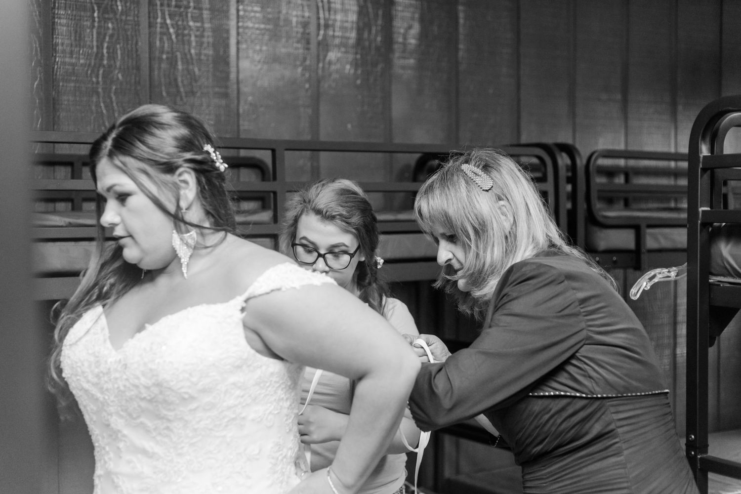 A wedding party helps adjust the bride's white lace dress in a candid moment.
