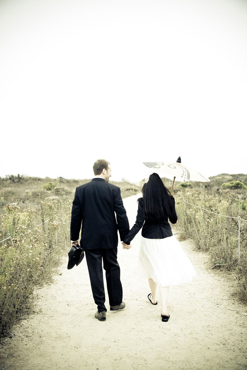 Couple walking down dirt path holding hands in formal attire.