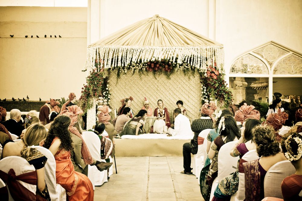 A wedding ceremony setup under a decorated tent canopy with guests seated around tables.