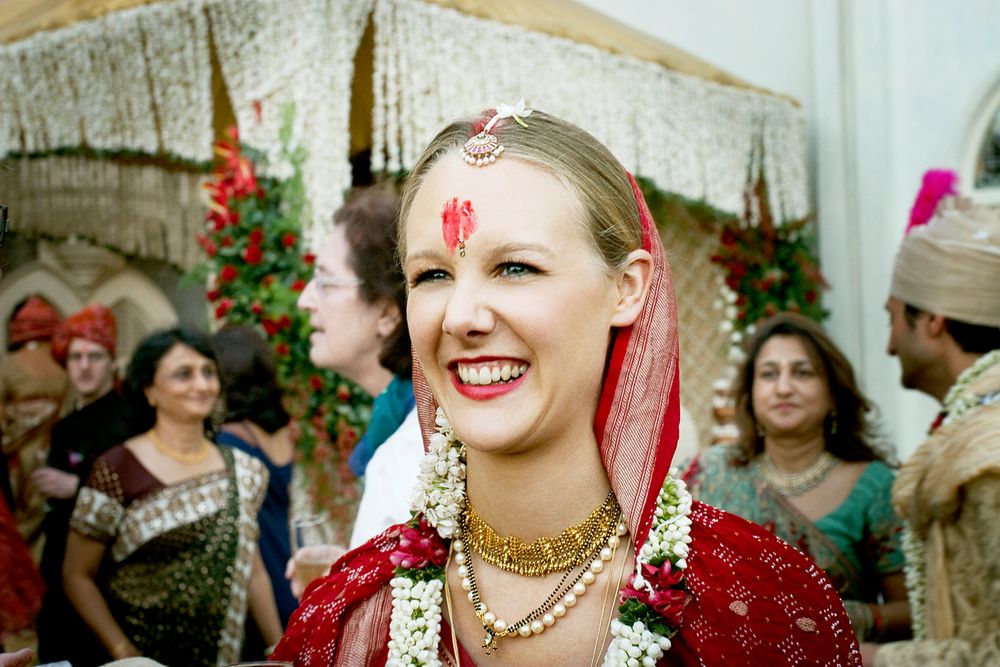 A bride wearing traditional Indian wedding jewelry and decorations smiles during her celebration.