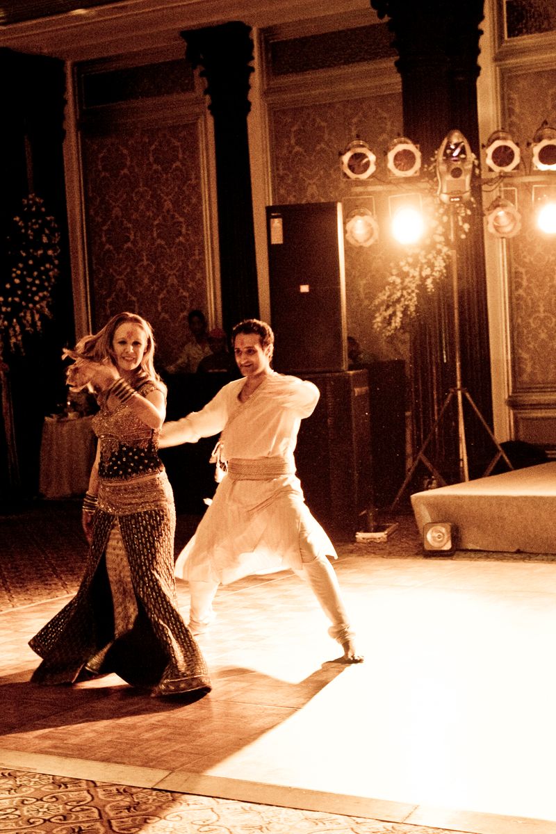 A couple performs an energetic dance routine at their wedding reception in warm sepia tones.