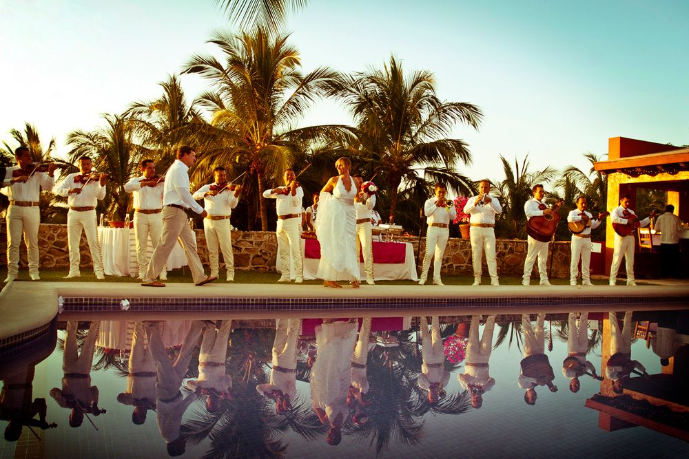 Wedding party lined up by a pool creating mirror reflections in the water at sunset with palm trees.