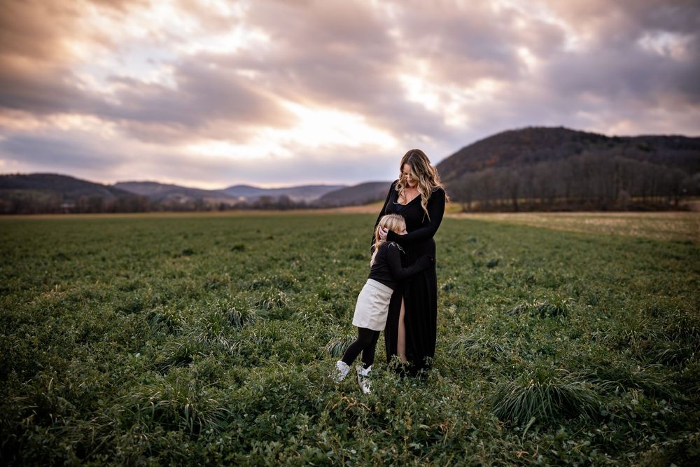 Couple embracing in a meadow during sunset with mountains in the background.