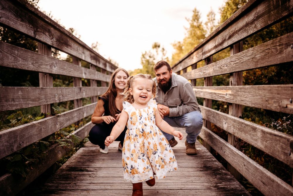 Family playtime on wooden bridge walkway during golden sunset.