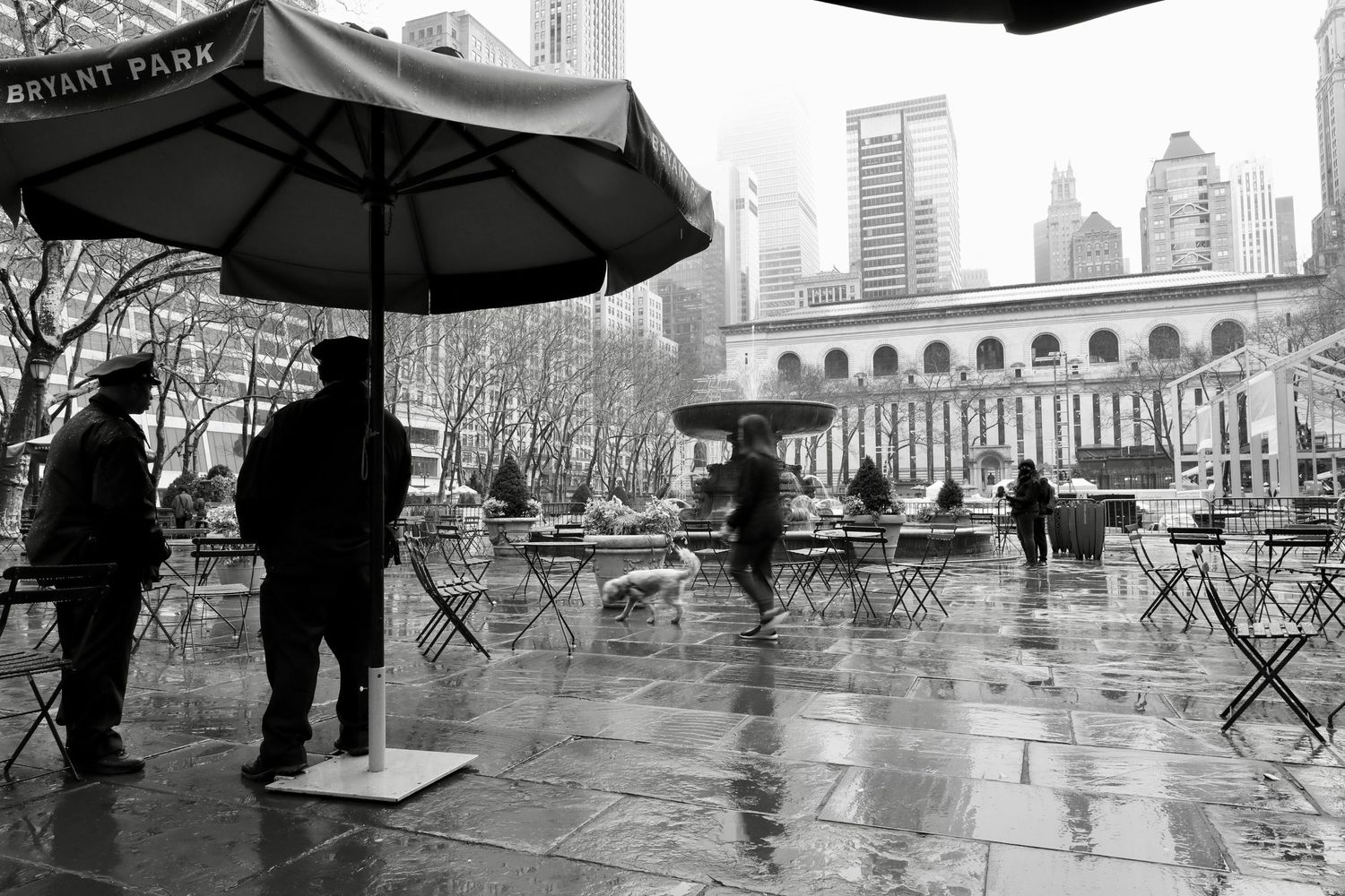 Rainy day scene in Bryant Park with umbrellas and people gathered under stormy skies.
