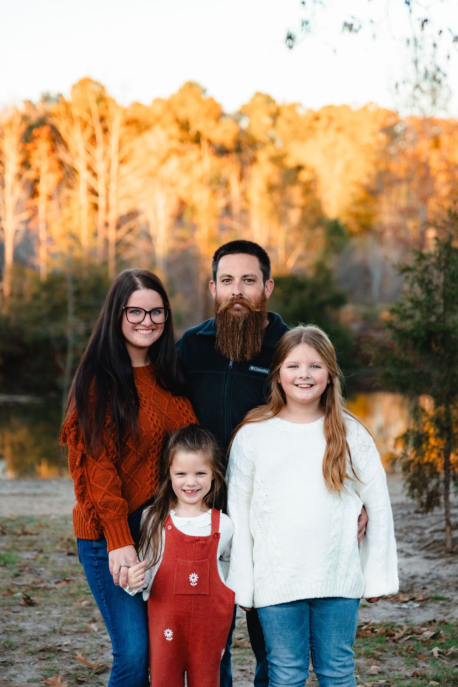 Outdoor family portrait at sunset with autumn colors and a lake backdrop.