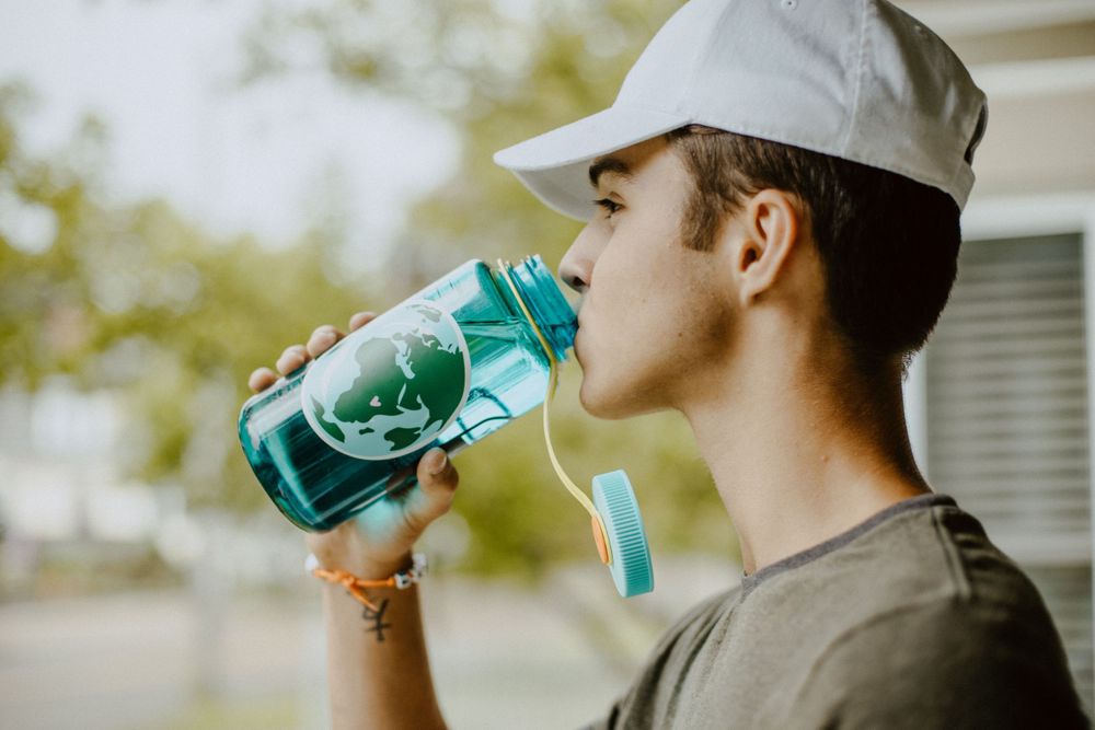 Someone drinking from a green water bottle while wearing a baseball cap.