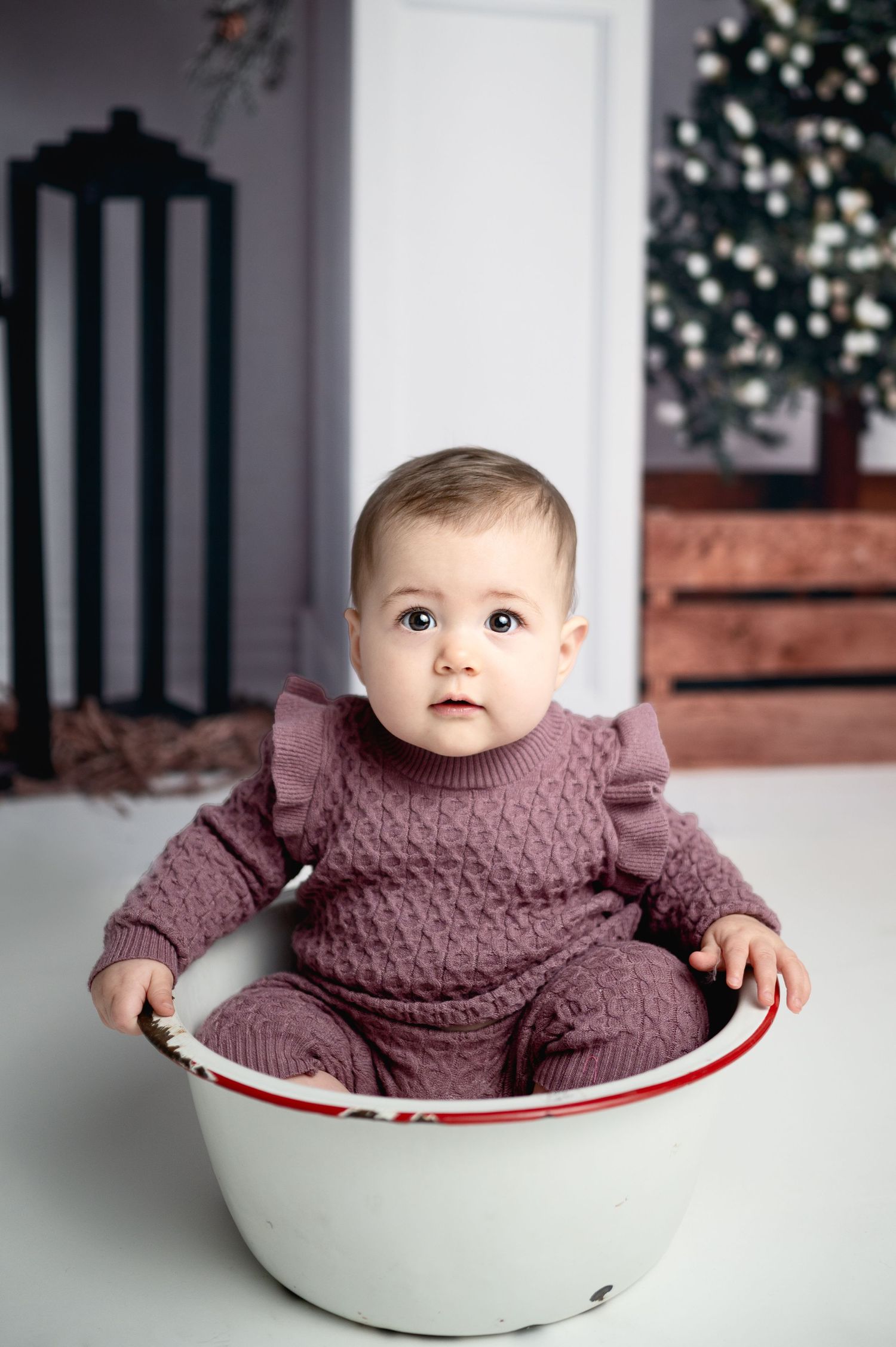 Baby in mauve sweater sitting in vintage white enamel bowl.