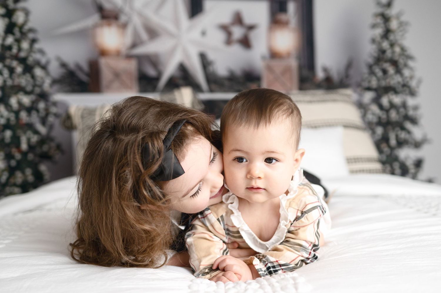 Winter family photo shoot with Christmas trees and white decor in a cozy indoor setting.